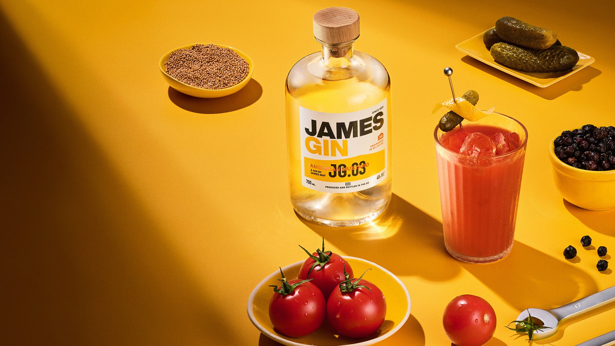 James Gin American Mustard bottle with a cocktail and garnishes on a yellow background. Award winning gin by James May.