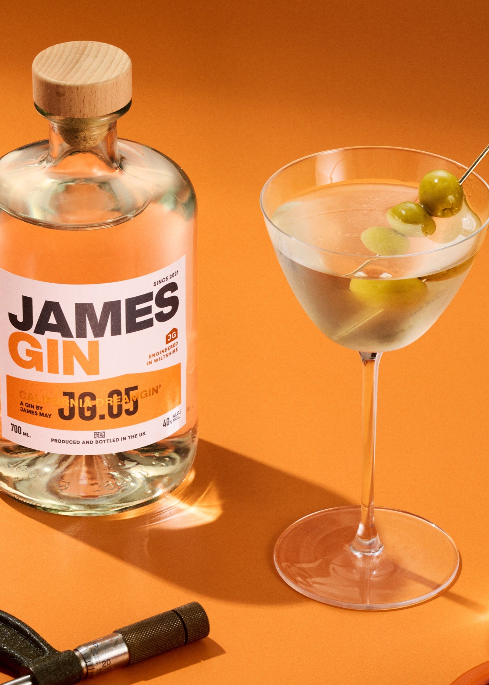 A James gin bottle California dreamgin' alongside a dirty martini with olives and a callipers measuring a mushroom