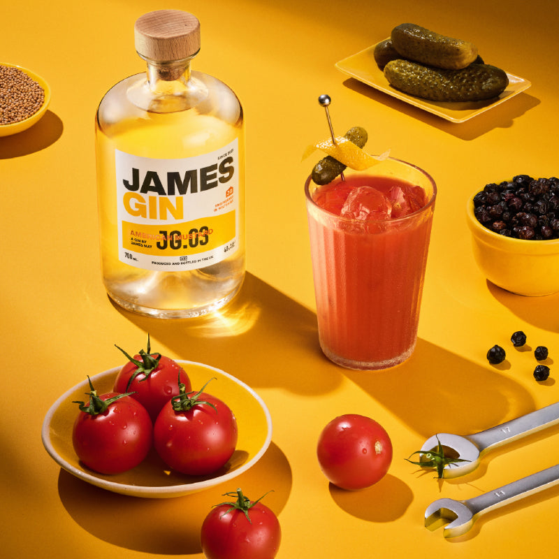 Bottle of James Gin American Mustard with a cocktail and garnishes on a yellow background. Award Winning Gin by James May